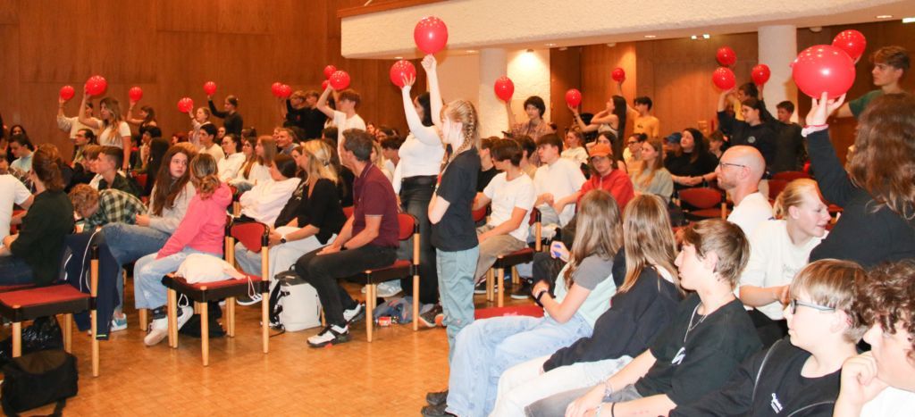 Publikum beim Wissenschaftsfest; einige Personen halten einen roten Luftballon in die Höhe